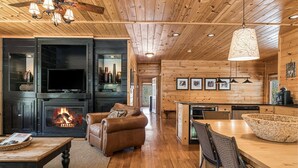 A cozy cabin interior with a fireplace, leather sofa, dining table, and kitchen area. - A Blessing An Upscale Mountain Getaway (Bryson City)