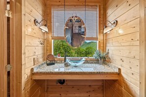 A wooden cabin bathroom with a granite countertop, a glass bowl sink, and a large mirror. - A Blessing An Upscale Mountain Getaway (Bryson City)