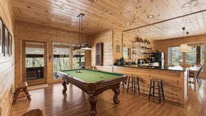 A wooden interior with a pool table, bar stools, and a kitchen area. - A Blessing An Upscale Mountain Getaway (Bryson City)