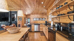 A modern kitchen with wooden walls, a dining area with a wooden table and chairs, and a fireplace. - A Blessing An Upscale Mountain Getaway (Bryson City)