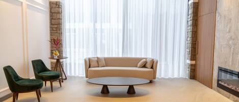Una sala de estar moderna con un sofá color beige, dos sillones verdes, una mesa redonda y una pared de acento de piedra.