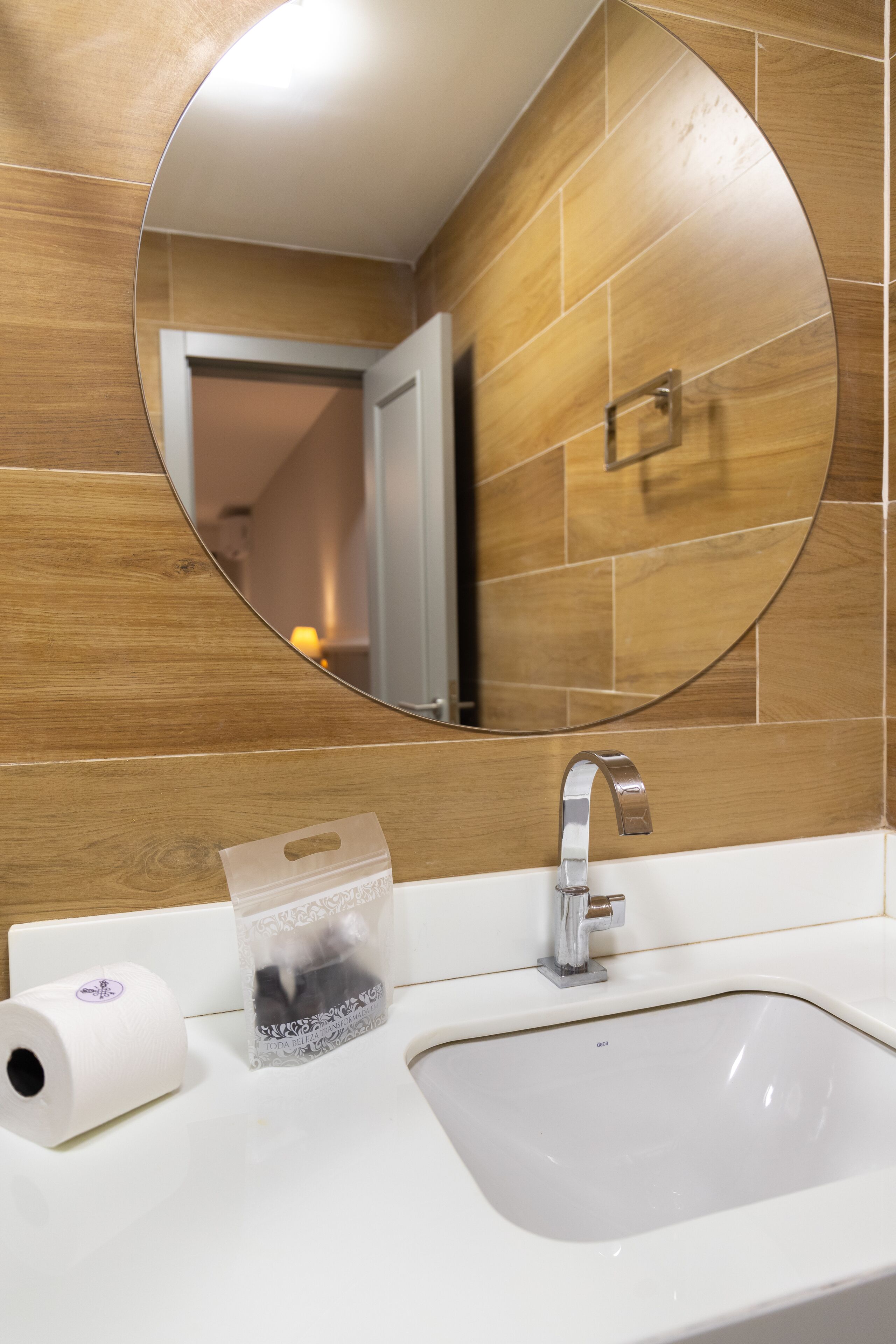 Un baño con un espejo redondo, un lavabo blanco y una pared de madera.