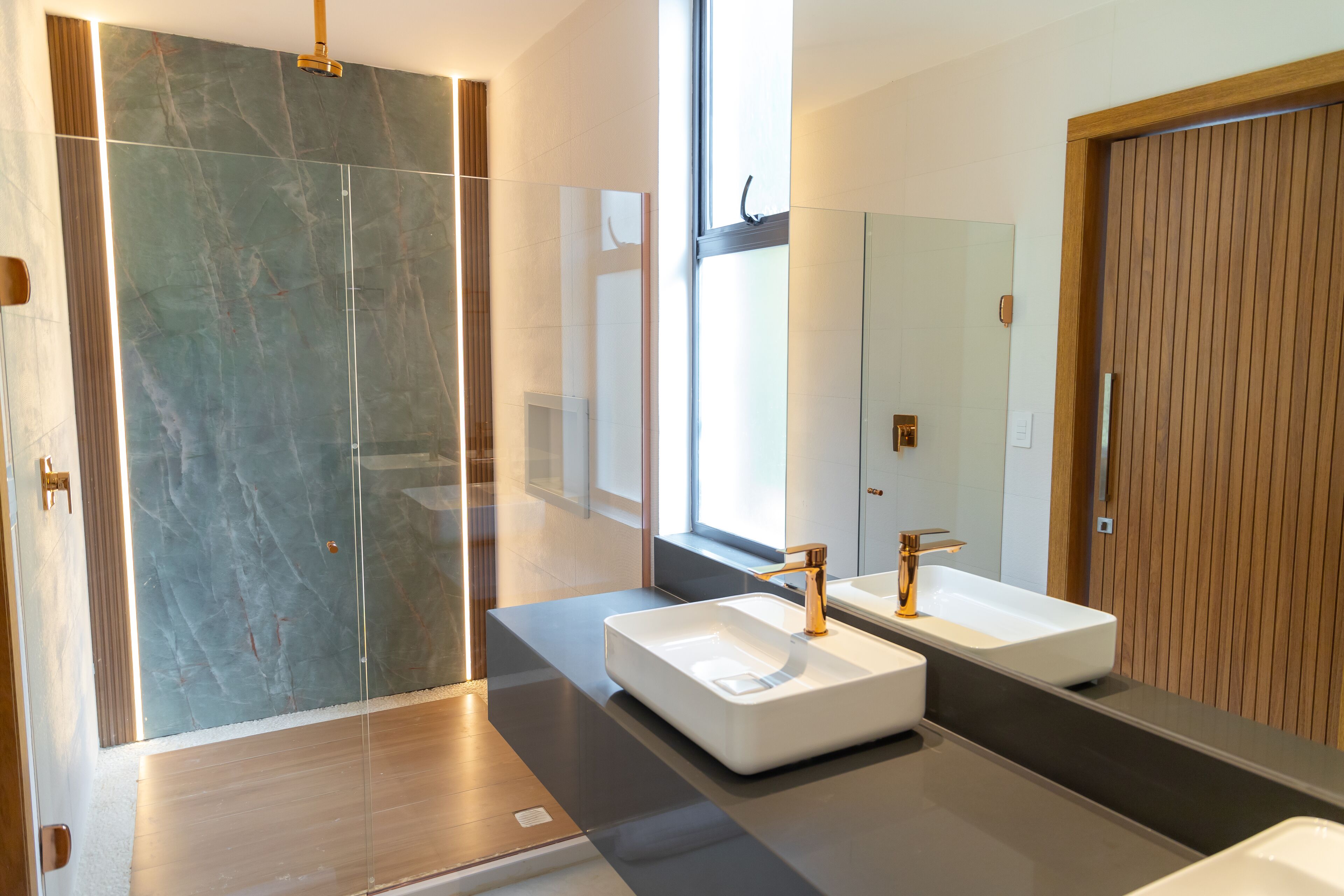 Une salle de bain moderne avec une douche à parois de verre, deux vasques dotées de robinets dorés et un grand miroir.