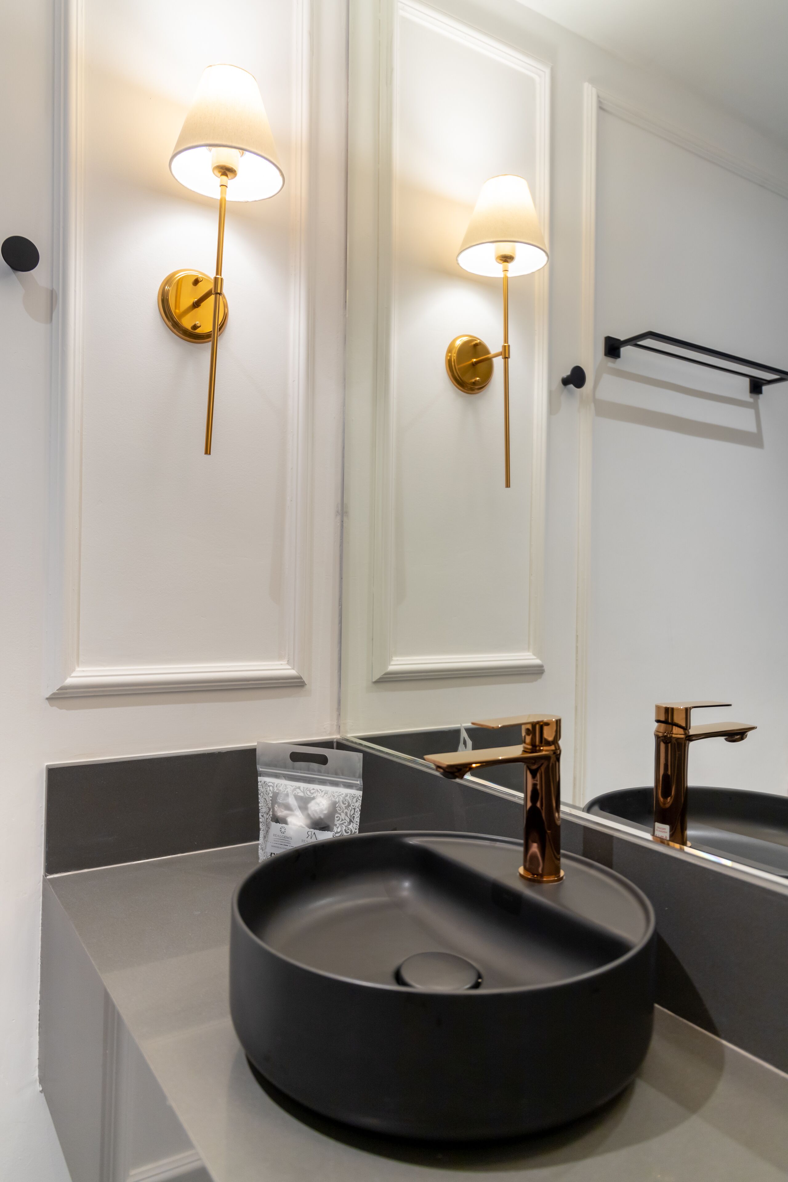 Een moderne badkamer met een zwart wastafel, gouden details en wandlampen.