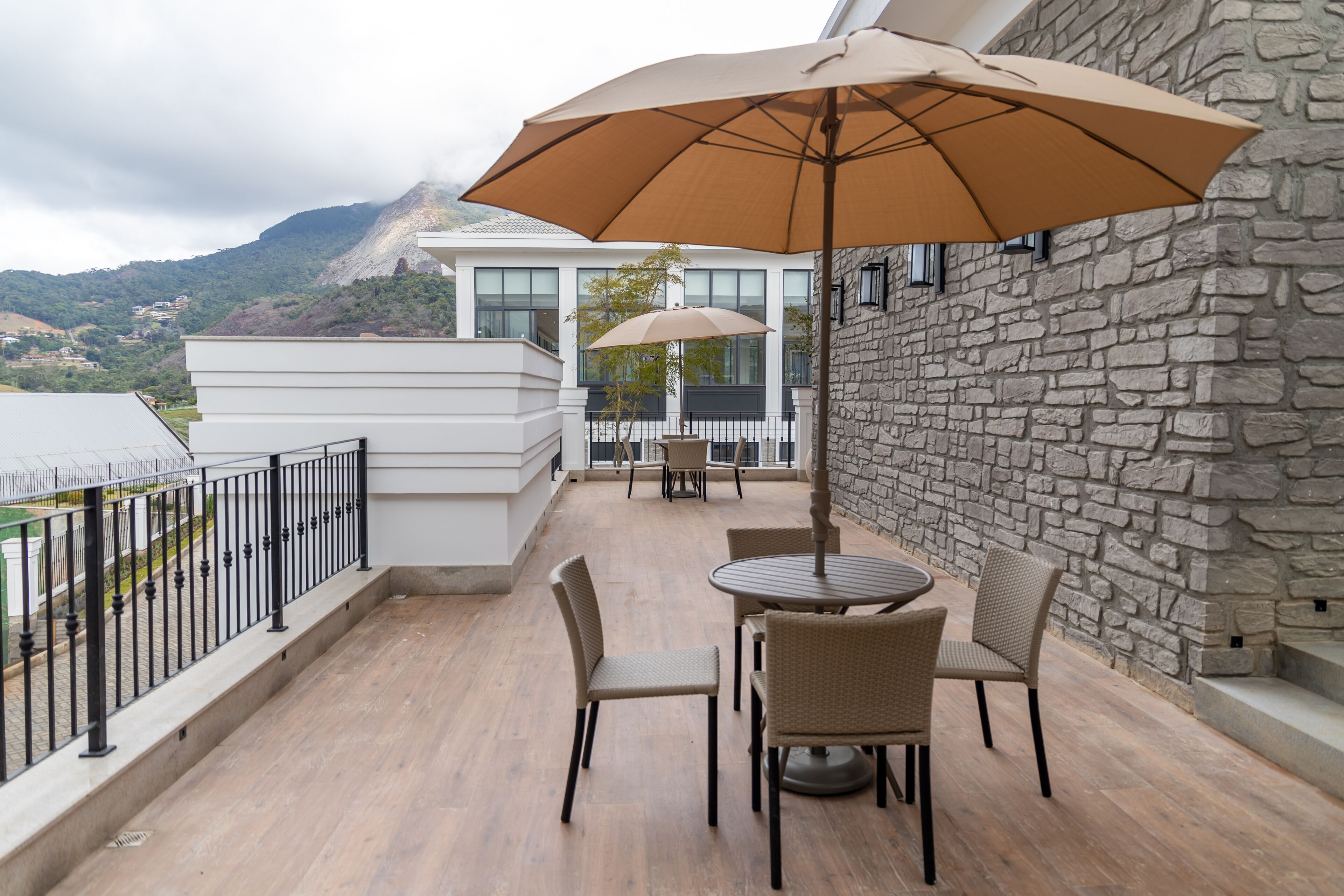 Een balkon met een tafel, stoelen en een grote parasol, tegen een stenen muur.