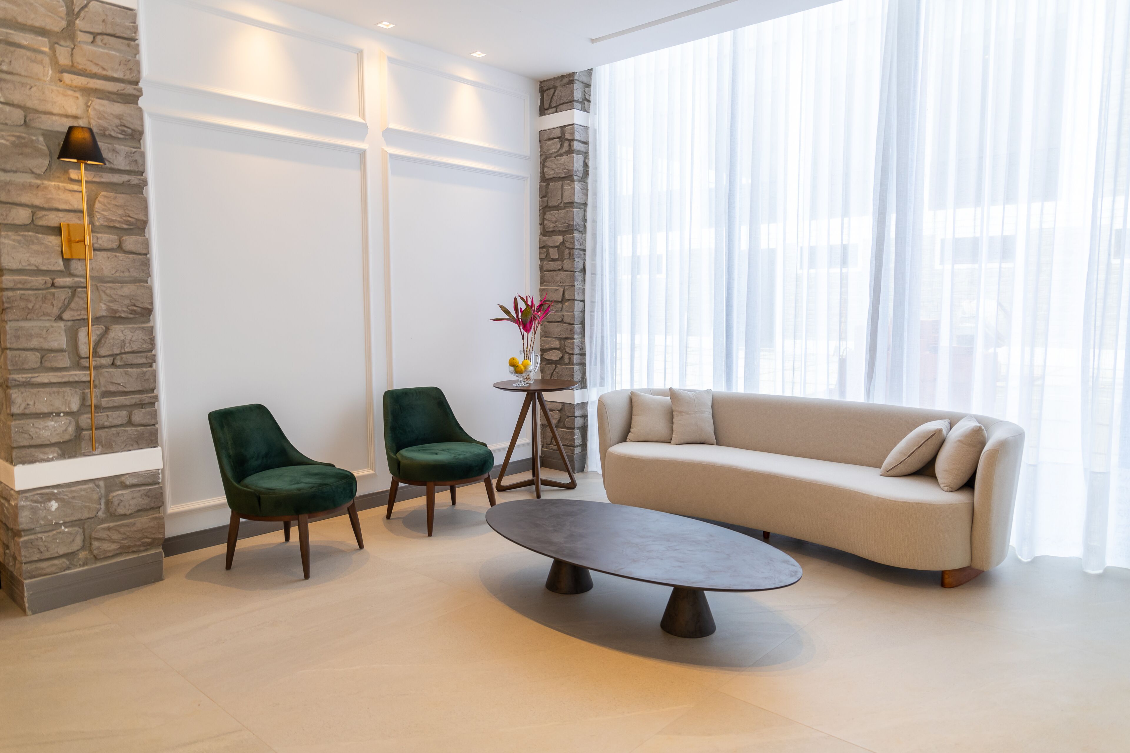 A modern living room with a stone accent wall, a beige sofa, two green armchairs, and a round coffee table.