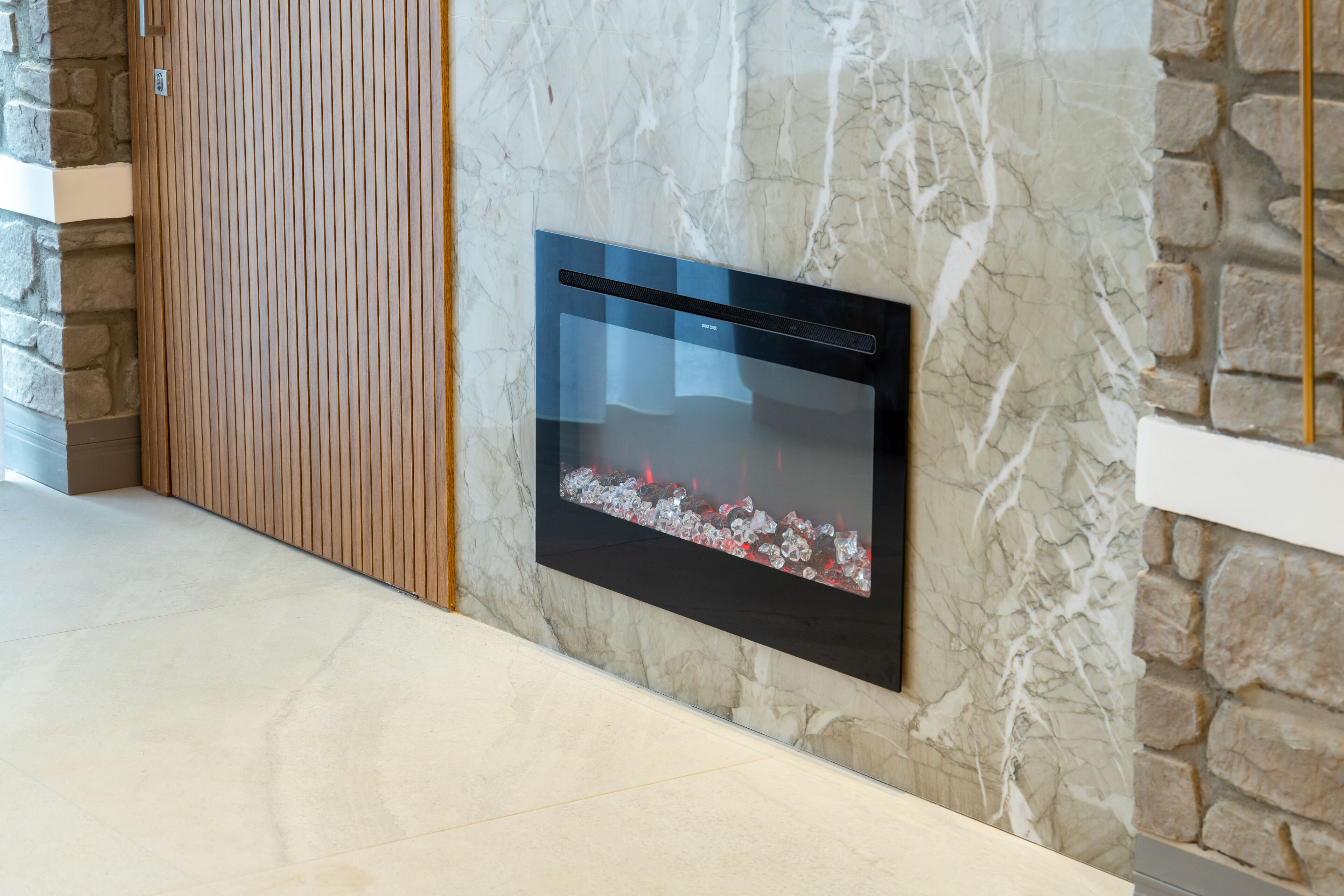 A modern fireplace with a glass front, set in a stone wall with a wooden panel on the left.
