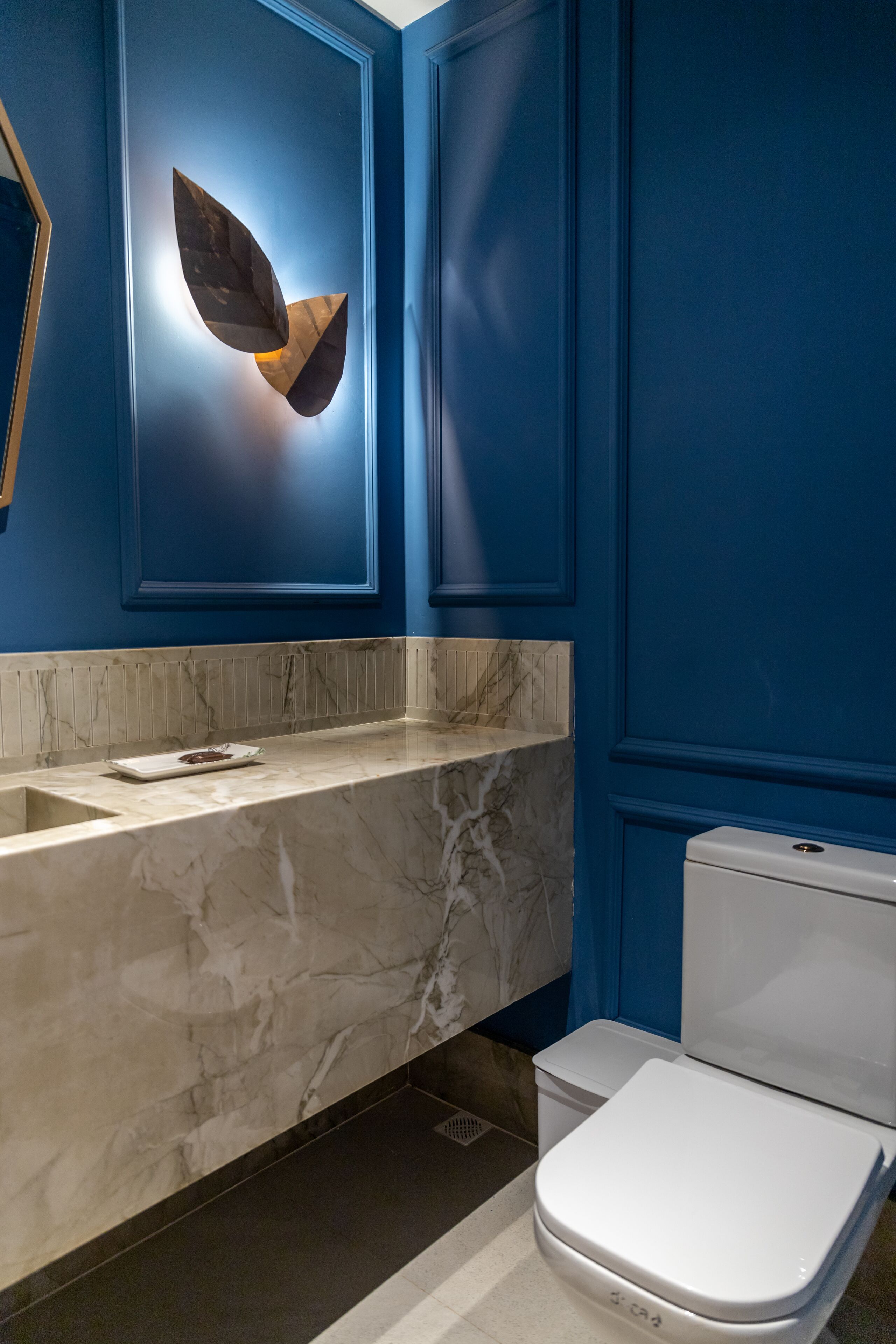 A bathroom with a marble sink, a white toilet, and a blue wall with a leaf-shaped light fixture.