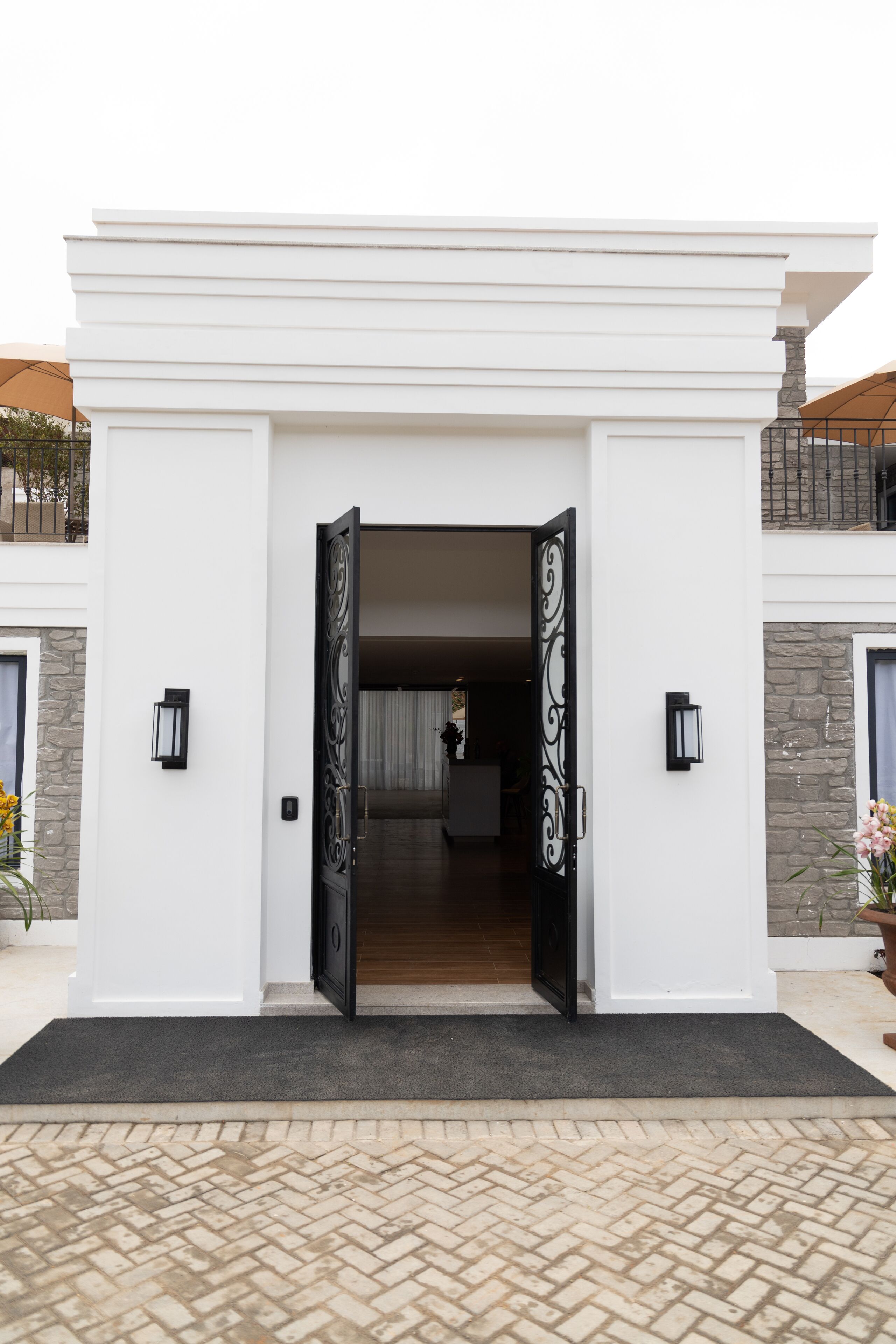 Une entrée moderne, caractérisée par une grande porte ouverte, un portail en métal noir et deux appliques murales.