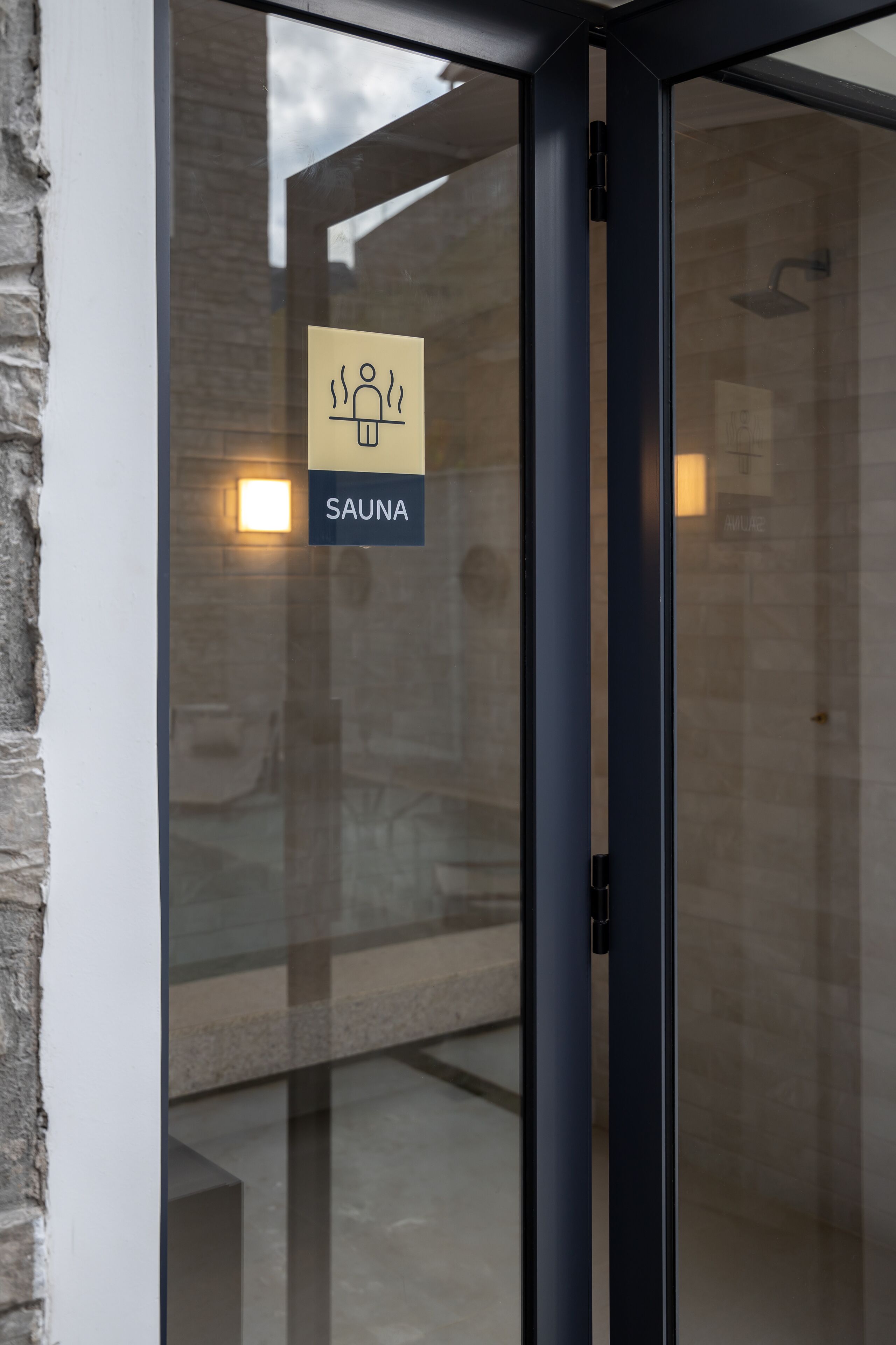 Une porte en verre avec une pancarte indiquant la présence d’un sauna.