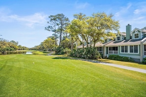 A golf course with a clubhouse, surrounded by trees and a clear sky.