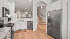 A modern kitchen with white cabinetry, stainless steel appliances, and a wooden staircase leading to a second floor. - 417 Wahoo Drive (Fripp Island)