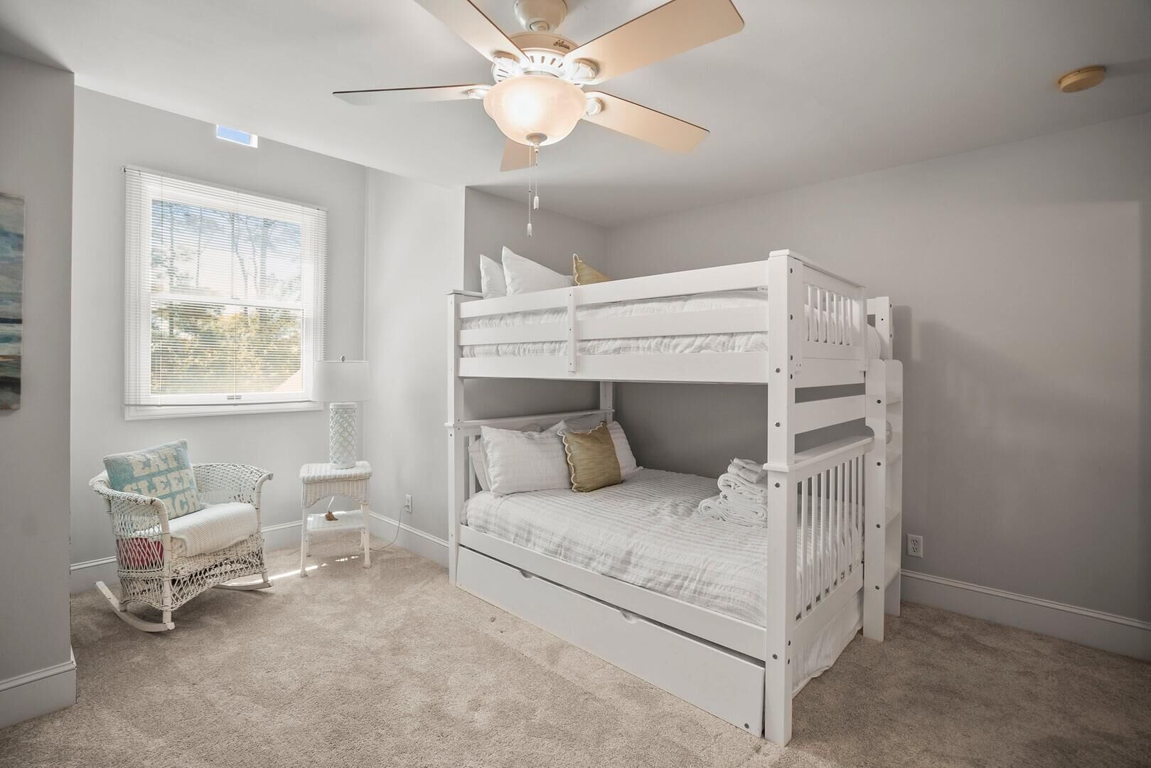 A bunk bed with a ceiling fan, a window with blinds, and a wicker chair.