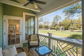 A porch with a dining table and chairs, a wicker chair, and a glass table.
