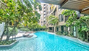 A swimming pool with a tiled deck, surrounded by greenery and modern buildings.