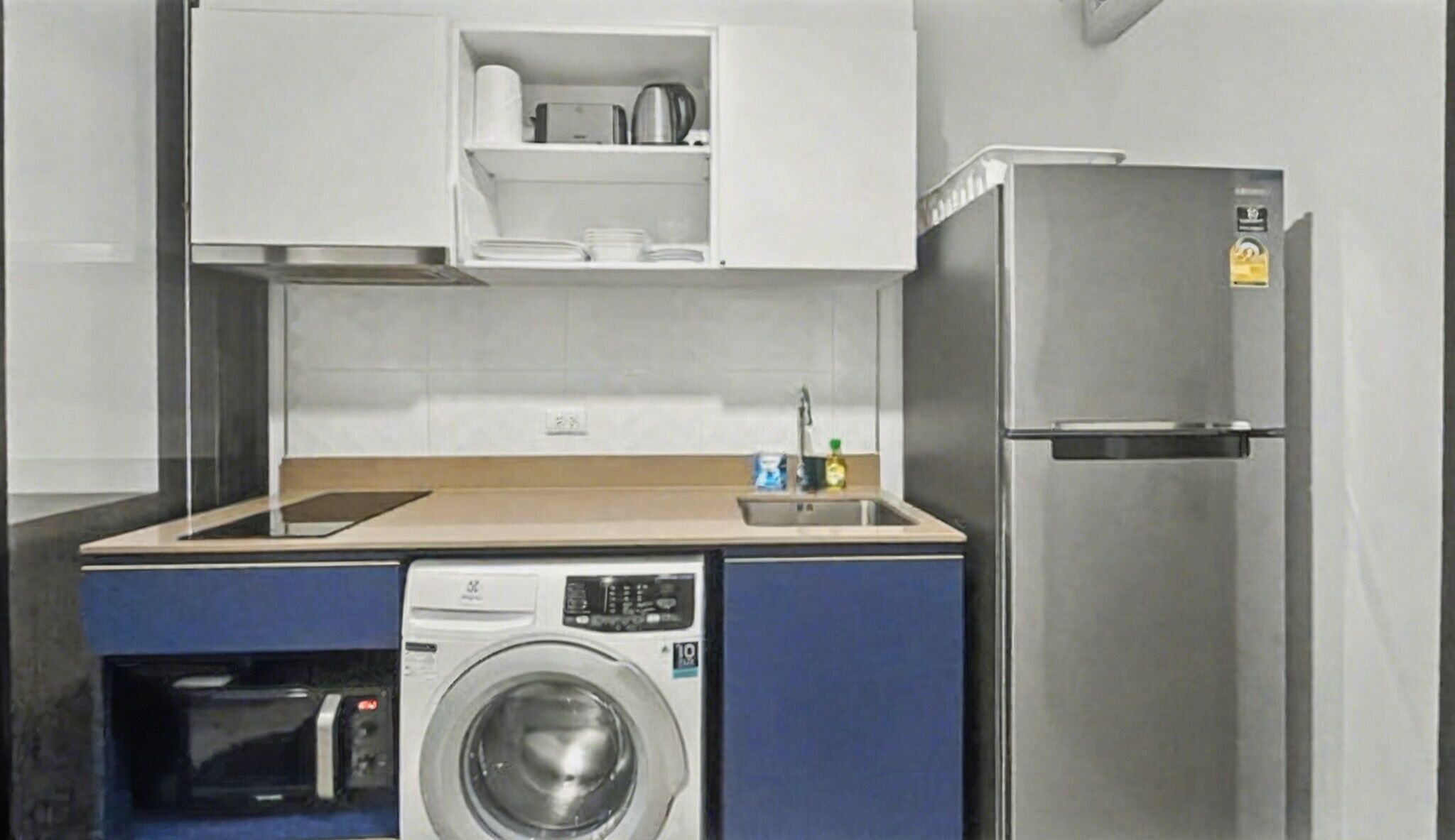A compact kitchen with a washing machine, a refrigerator, and a microwave.