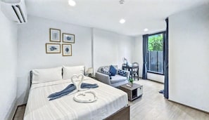A modern hotel room with a bed, a sofa, a small table, and a window.