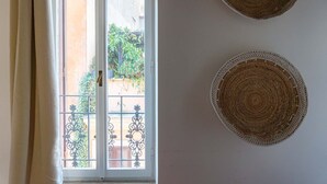 A room with a view through a door to an outdoor area with greenery and a railing. There are two woven wall hangings on the wall. - Cozy Flat near Castel S. Angelo (Rome)