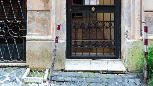 A building with a black metal gate, a window with a metal grill, and a stone wall with the number 16. - Cozy Flat near Castel S. Angelo (Rome)