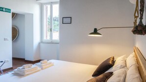 A hotel room with a bed, a bedside lamp, a window, and a sign indicating an emergency exit. - Cozy Flat near Castel S. Angelo (Rome)