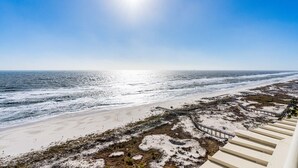 A beach view with a wooden boardwalk leading to the water, sandy beach, and dunes. - Gulf-Front Condo with Huge Balcony, Panoramic Views & 3 King Beds (Gulf Shores)
