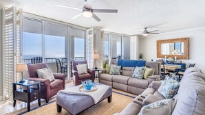A spacious living room with a view of the ocean, a ceiling fan, and a dining area with a table and chairs. - Gulf-Front Condo with Huge Balcony, Panoramic Views & 3 King Beds (Gulf Shores)