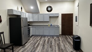 Una cocina con armarios grises, un refrigerador negro, piso de madera y un reloj en la pared.