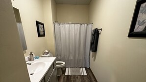 Un baño estrecho con suelo de madera, un lavabo blanco, un inodoro y una cortina de ducha.