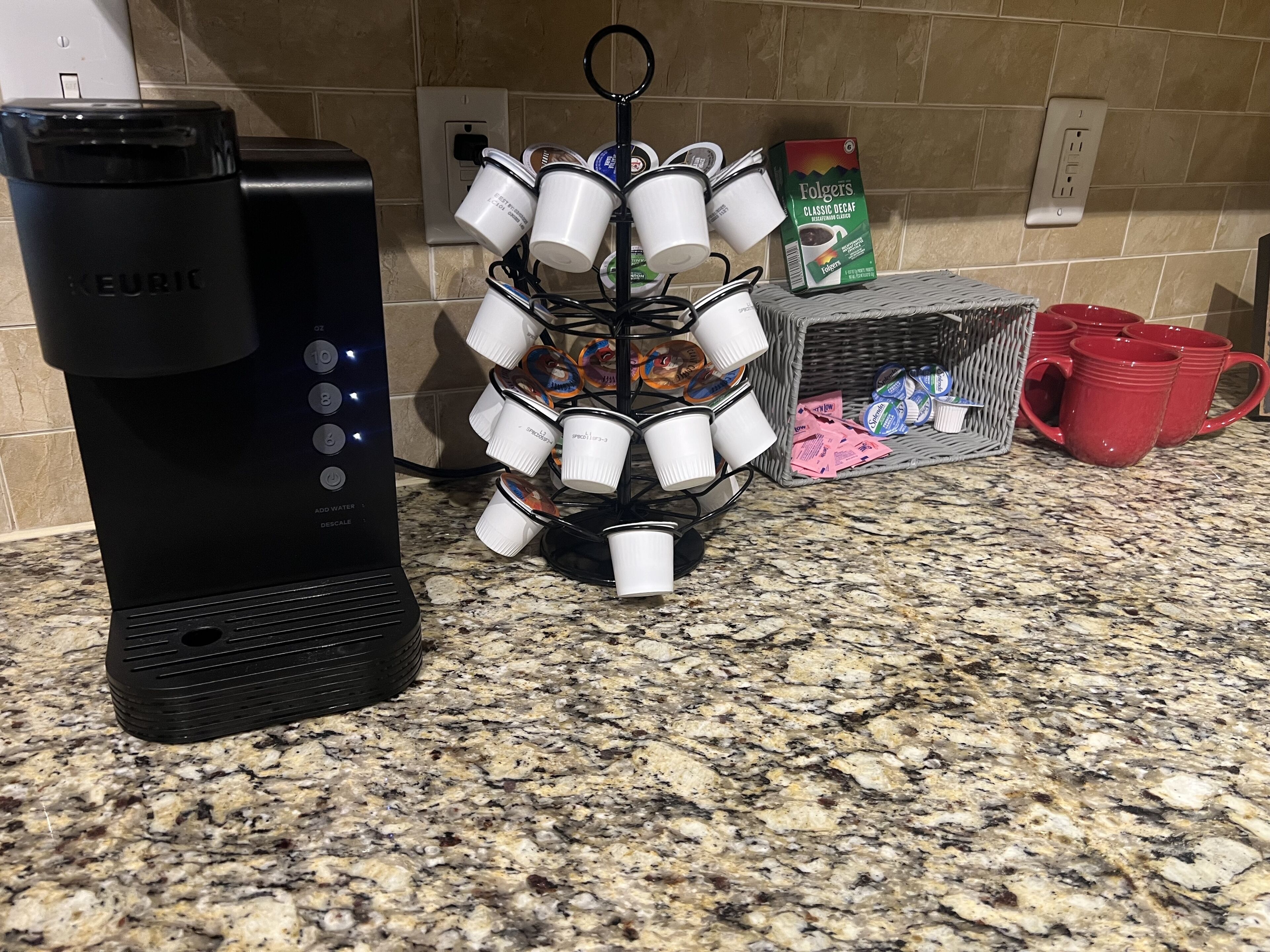 A coffee maker, a mug holder, and a box of Folgers coffee on a kitchen counter.