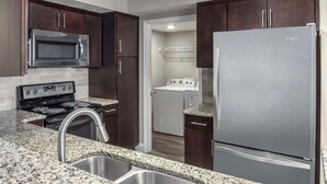Una cocina moderna con armarios de madera oscura, electrodomésticos de acero inoxidable, encimeras de granito y un lavamanos doble.
