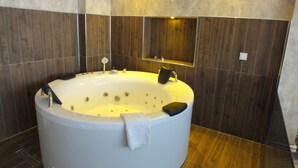 A modern bathroom with a large freestanding bathtub, a mirror above it, and dark wooden paneling on the walls. - ÇANKAYA SUIT HOTEL (Ankara)