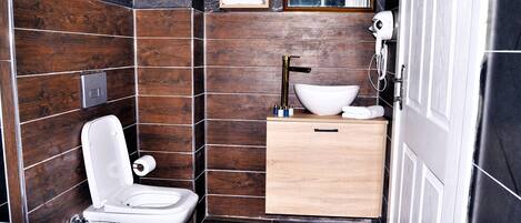Un baño moderno con inodoro blanco, un lavabo grande y un mueble de tocador de madera.