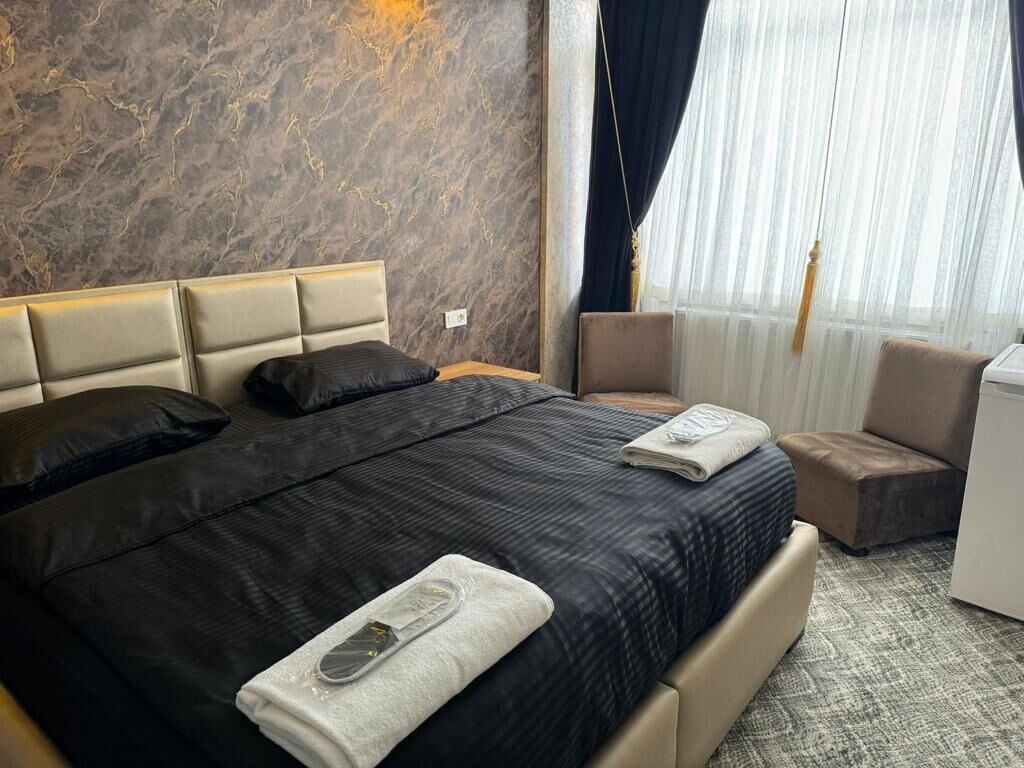 A hotel room with a bed, a chair, a small table, and a window with curtains.