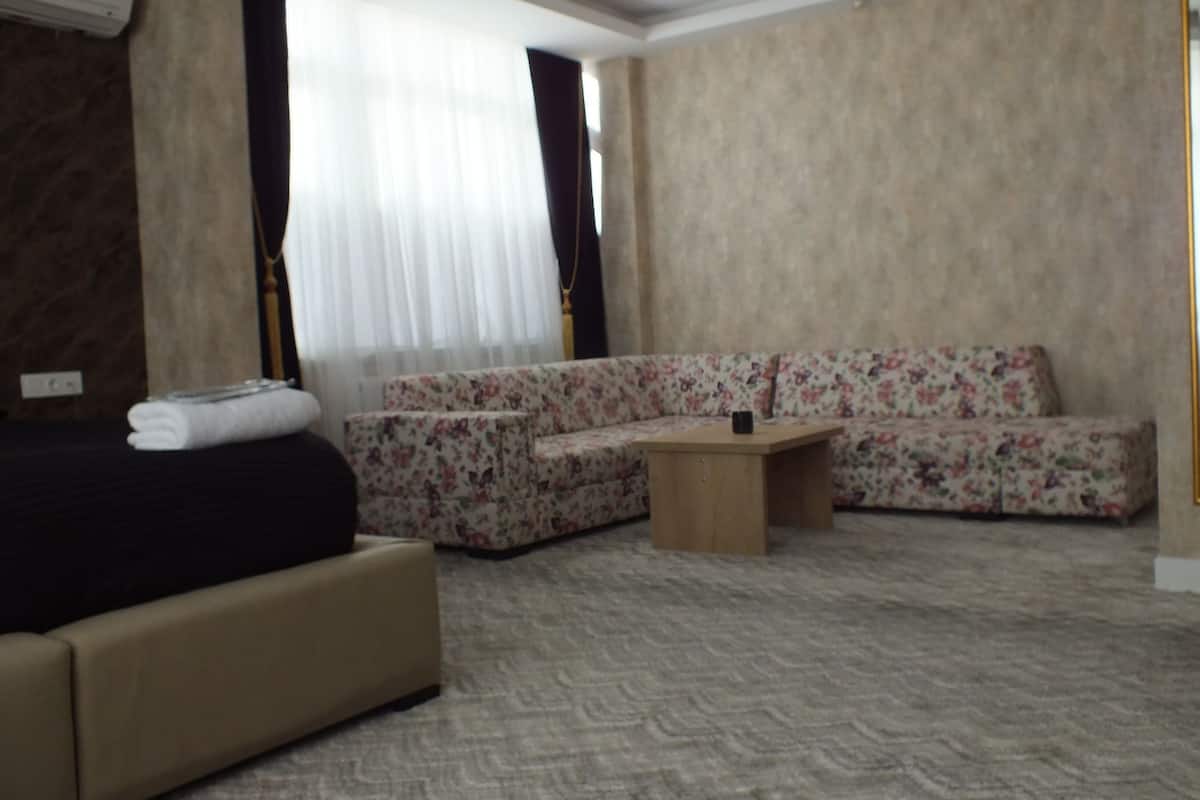 A hotel room with a bed, a sofa, a small wooden table, and a window with sheer curtains.