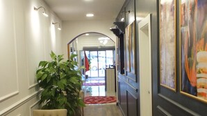 A hallway with a wooden floor, a potted plant, a chair, and framed artwork on the walls. - ÇANKAYA SUIT HOTEL (Ankara)