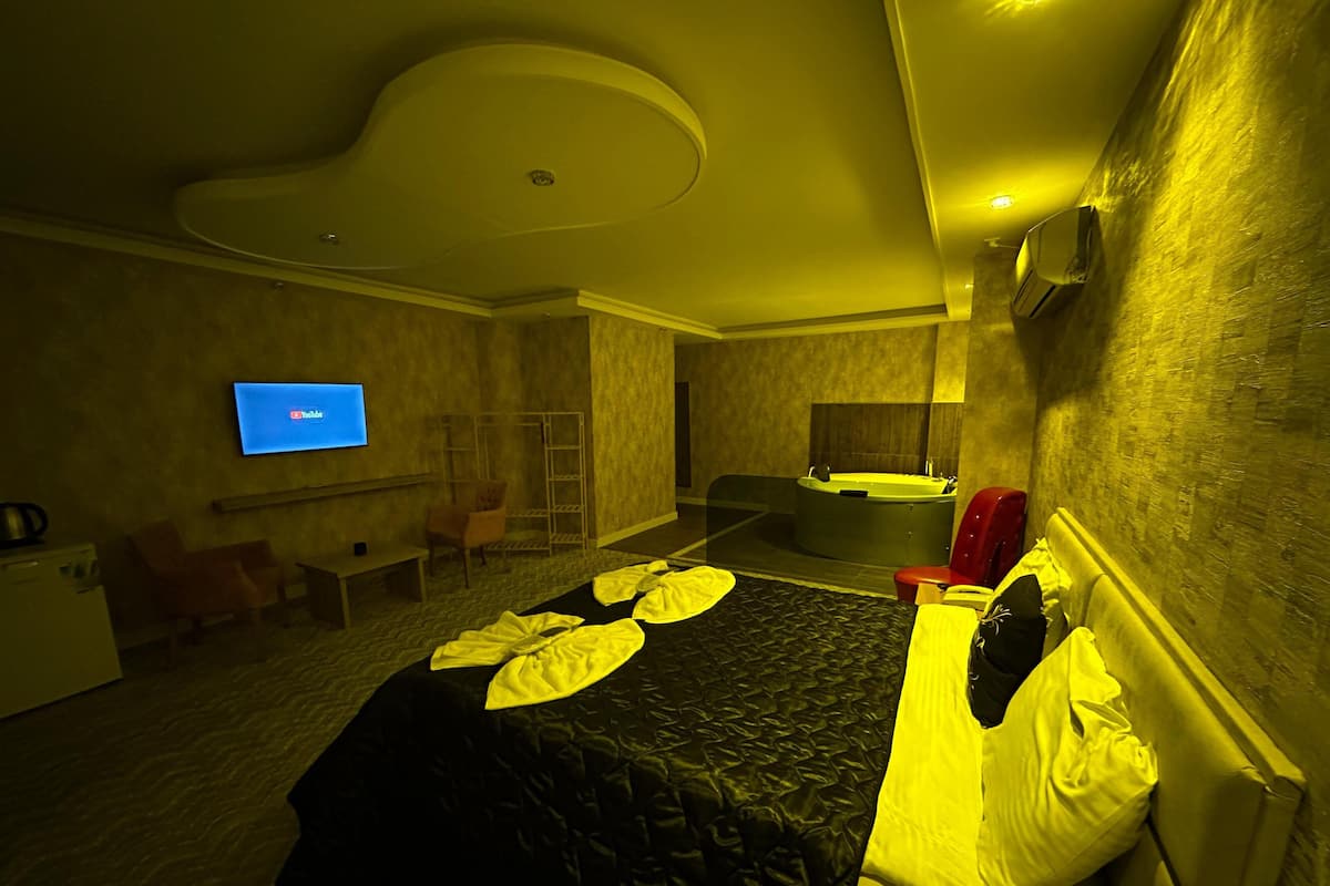 A hotel room with a bed, a TV, a desk, a chair, a red chair, a bathtub, and a small table.