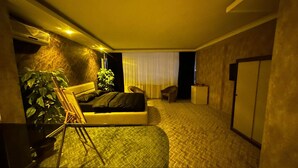 A hotel room with a bed, a small desk, a chair, a potted plant, and a wardrobe. - ÇANKAYA SUIT HOTEL (Ankara)