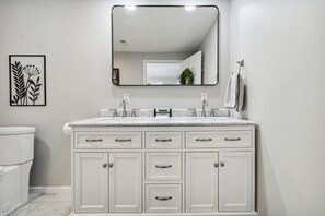 A bathroom with a white vanity, a large mirror, and a framed botanical print on the wall.
