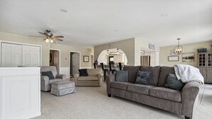 A spacious living room with a grey sofa, beige armchairs, and a white entertainment unit.