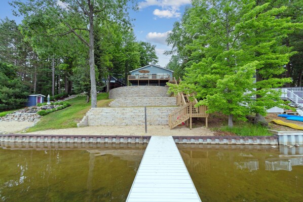 A house with a dock leading to a pond, surrounded by trees and a white fence.