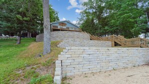 A stone retaining wall with a wooden staircase leading to a building with a blue roof and a wooden deck.