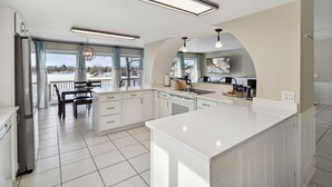 A modern kitchen with white cabinetry, a large island, and a view of the outdoors through large windows.