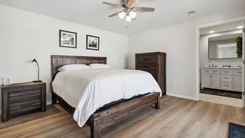 A bedroom with a wooden bed, a nightstand, a ceiling fan, and a bathroom with a sink and cabinets.