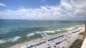 A beach with rows of blue umbrellas and beach chairs, a sandy shore, and the ocean.