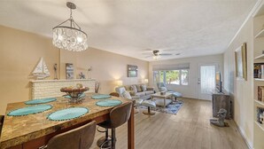 Un salon spacieux avec une cheminée, un coin repas avec une table et des chaises en bois, et un ventilateur de plafond.
