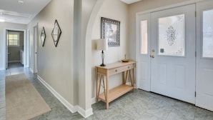 A hallway with a wooden console table, a door with decorative glass panels, and a wall with framed artwork.