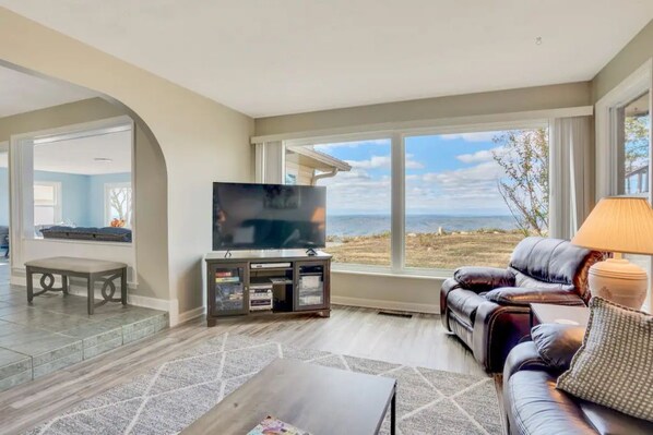 A living room with a large TV, leather sofa, and a view of the beach. - Vantage Point II (Rising Fawn)
