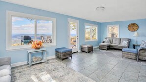 A spacious living room with large windows, a sofa set, and a small table with a vase of flowers.