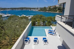 A rooftop pool with lounge chairs, a view of the sea, and surrounding greenery.