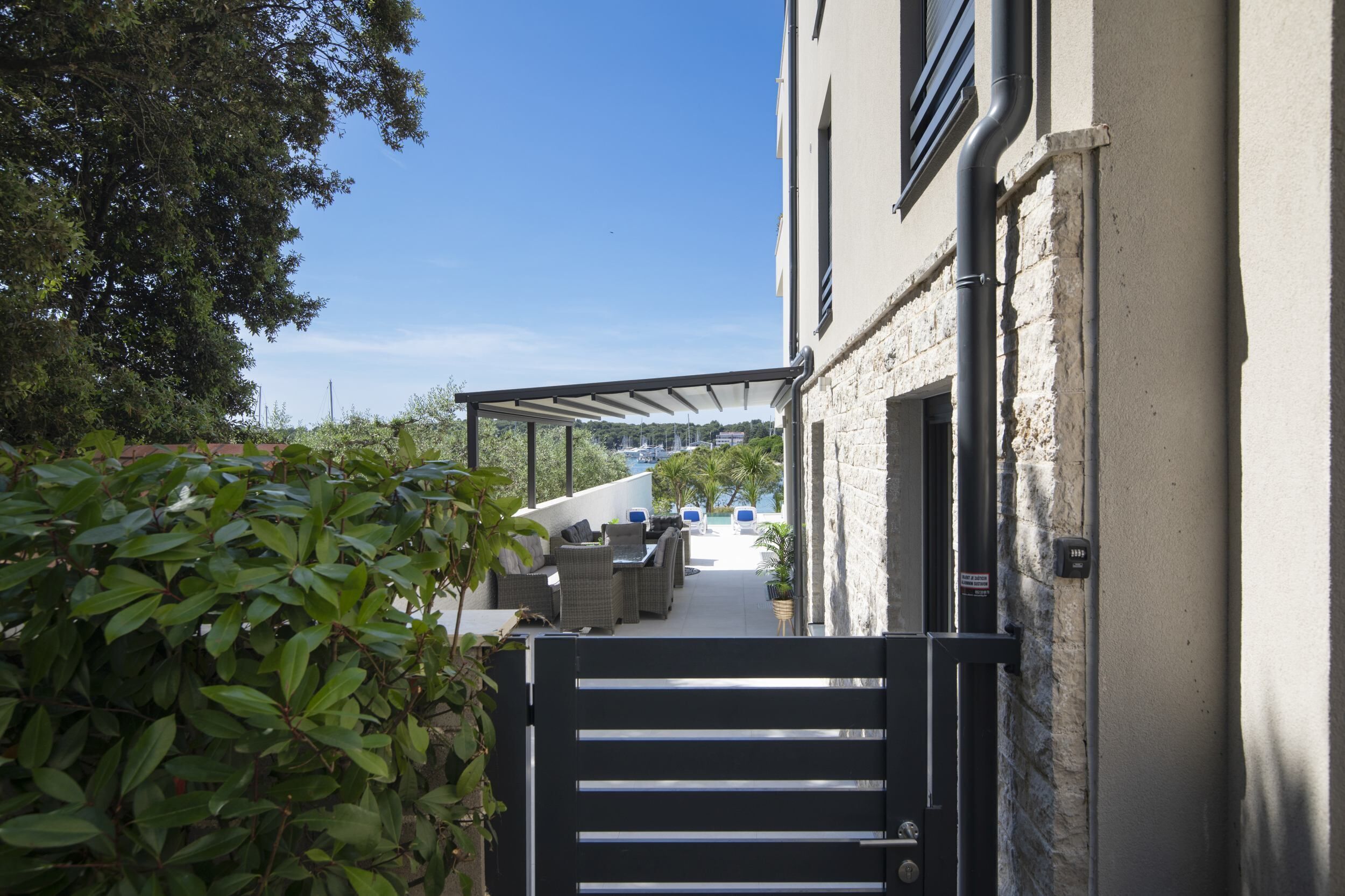 Un patio extérieur aménagé, accessible par un portail, avec des meubles d’extérieur, une pergola et une vue sur une piscine et des montagnes.